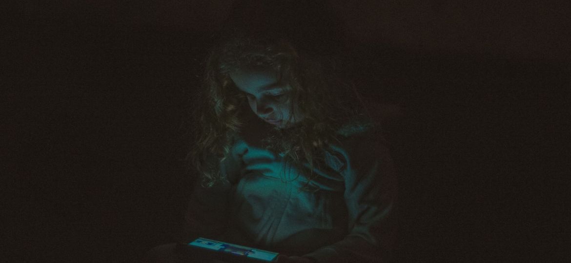 طفلة تستخدم جهاز إلكتروني في ظلام، ربما تعاني من إدمان الشاشات.