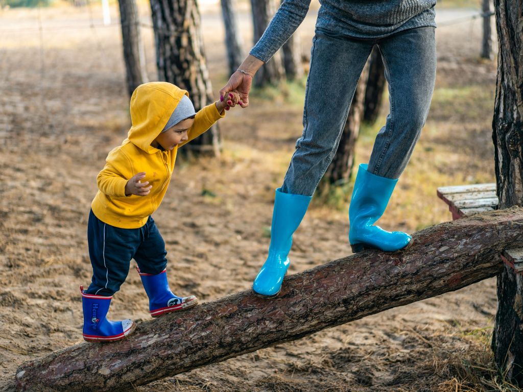 طفل في مرحلة الطفولة المبكرة يسير على جذع بمساعدة أحد والديه.