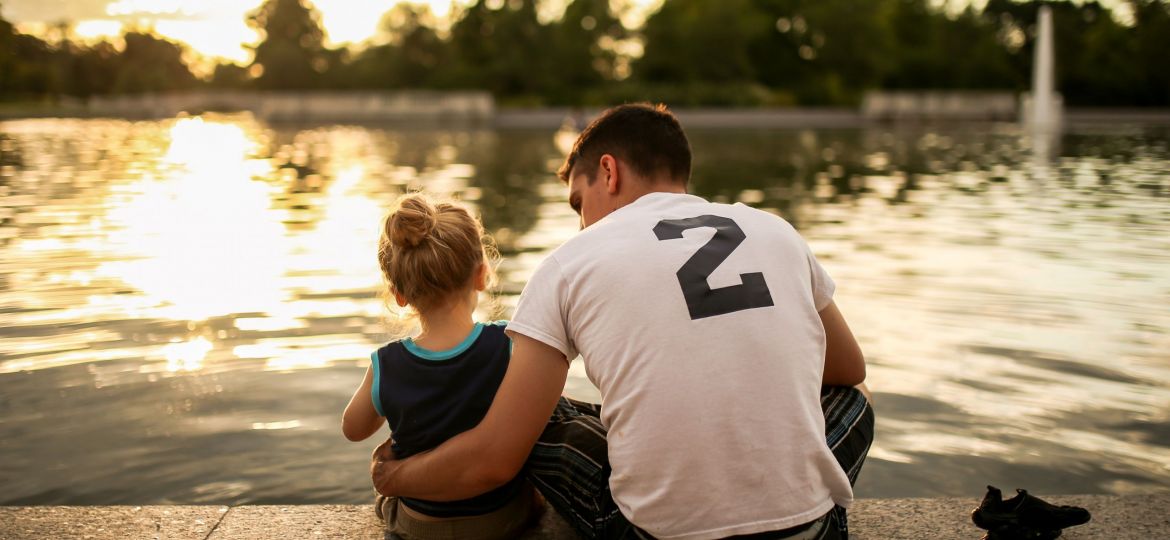 أب يجلس مع طفلته على ضفاف نهر، ويستمتعان بقضاء الوقت النوعي معًا