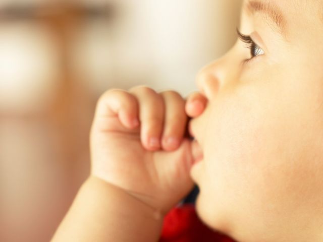 طفل صغير يضع إبهامه في فمه، كدلالة طبيعية لعادة مص الأصابع.